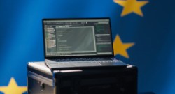 Un ordenador portátil sobre una caja de transporte y de fondo parte de la bandera de la Unión Europea